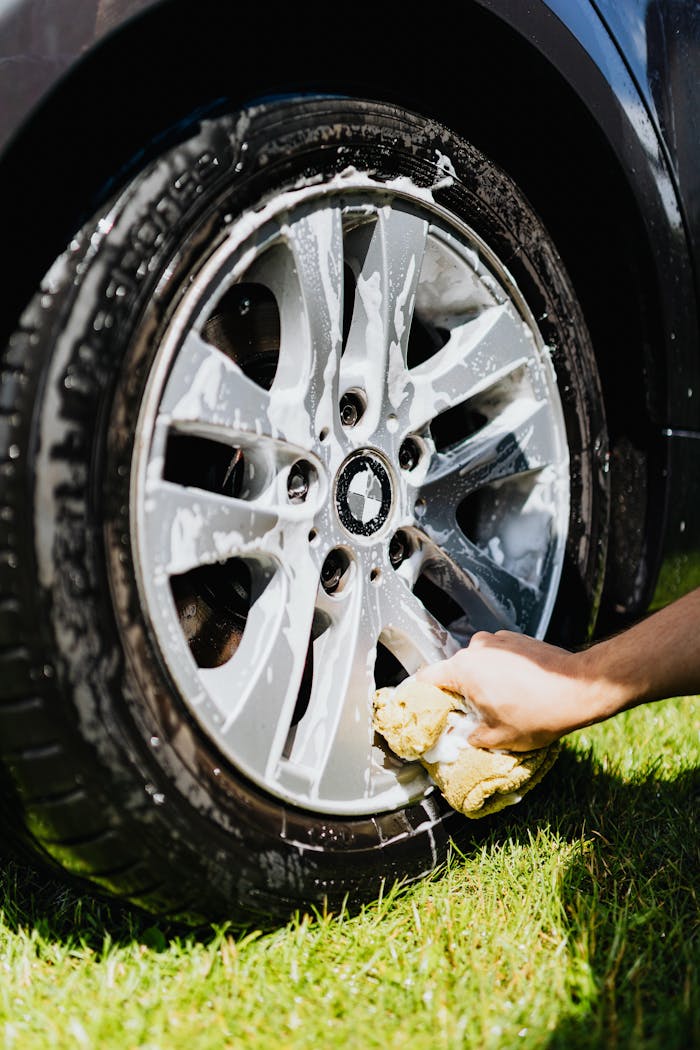 Close-up of a car wheel with soap suds and hand cleaning it on grass.