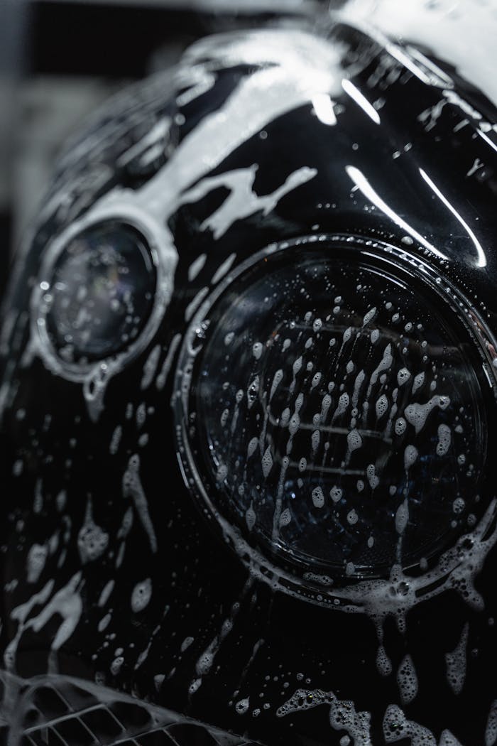 A detailed close-up of a car headlight covered with soap suds during a wash.